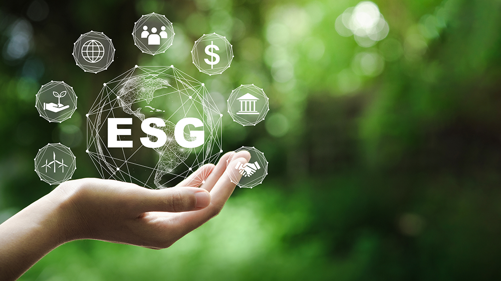 Eine Hand hält eine Grafik einer Weltkugel mit ESG-Icons vor einem grünen Hintergrund.