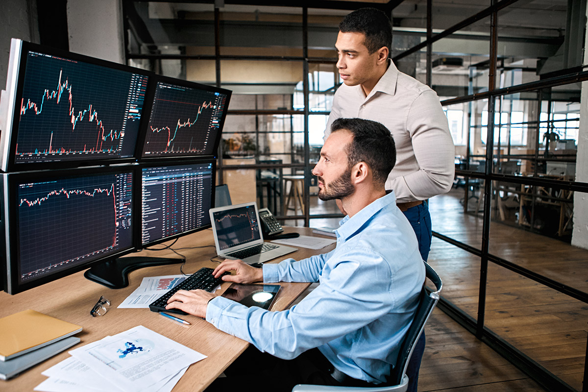 Zwei Kollegen beobachten gemeinsam am Computer Aktienkurse.